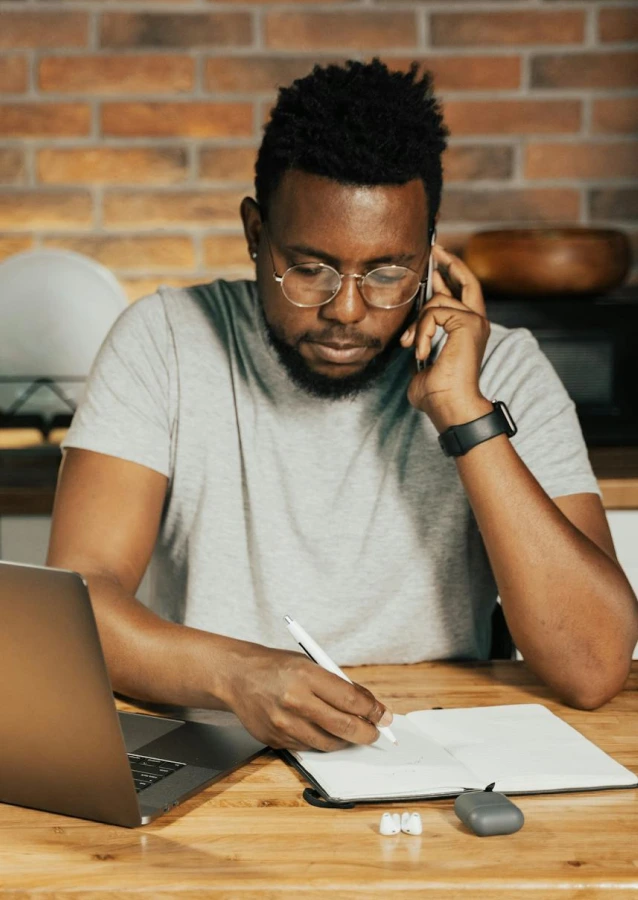 Someone on a call, taking notes beside a laptop